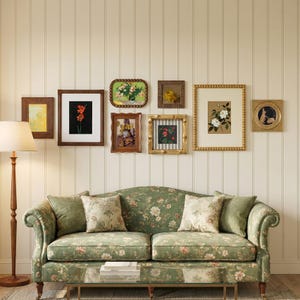 Peut inclure: Un salon avec un canapé vert à motifs floraux et des coussins assortis. Au-dessus, une collection d'œuvres d'art encadrées sur le thème floral et botanique est accrochée à un mur crème. Un lampadaire en bois se trouve à gauche.