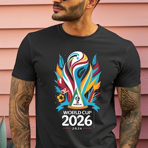 May include: Black t-shirt featuring a colorful graphic design for the 2026 World Cup. The design includes a stylized trophy, a soccer ball, and the text "WORLD CUP 2026". The shirt is a crew neck style.
