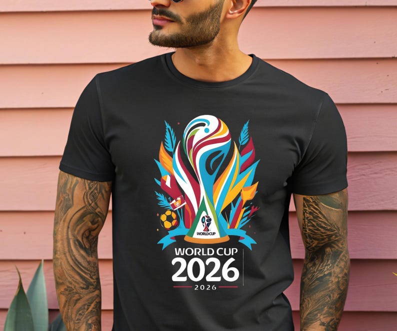 May include: Black t-shirt featuring a colorful graphic design for the 2026 World Cup. The design includes a stylized trophy, a soccer ball, and the text "WORLD CUP 2026". The shirt is a crew neck style.