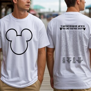 May include: White t-shirt featuring a large black outline of Mickey Mouse's head on the front. The back of the shirt has a word search puzzle with Disney-related words and the text: "TO ANYONE BEHIND ME, WE'RE IN THIS LINE TOGETHER. ENJOY!"