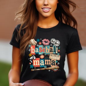 May include: Black t-shirt with a colorful graphic design featuring a baseball, lips, disco balls, and the words "baseball mama." The design includes stars, a megaphone, and a baseball bat.