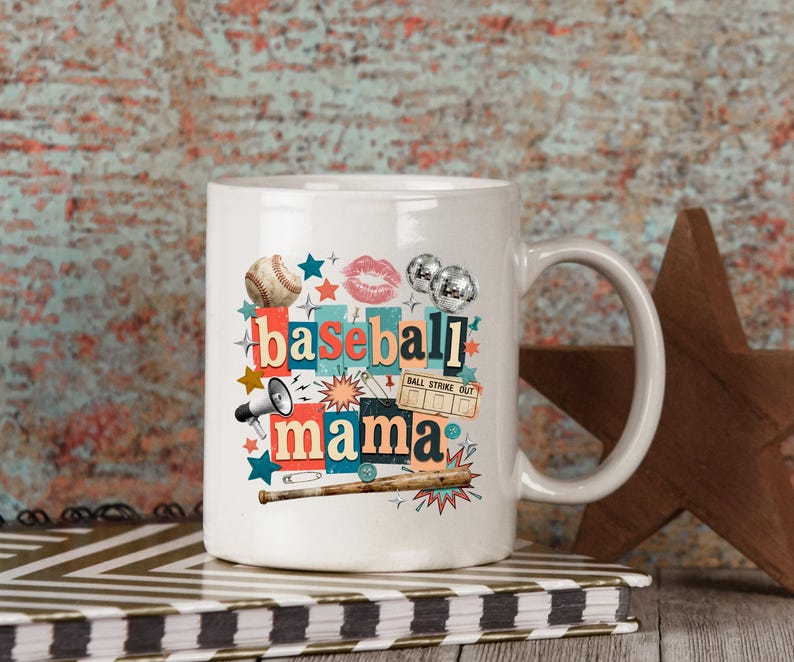 May include: White ceramic mug with the words "baseball mama" in a collage style design. The design includes a baseball, lips, stars, a megaphone, and a baseball bat. The mug is sitting on a notebook.