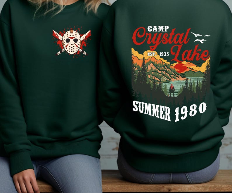 May include: Dark green sweatshirt with a graphic on the front of a hockey mask and crossed machetes. The back features a Camp Crystal Lake design with text that reads "Summer 1980".