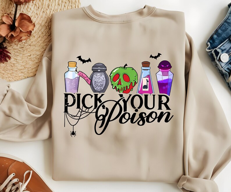 May include: Beige sweatshirt featuring a colorful graphic of potion bottles, a green apple with a skull design, and bats. The text "Pick Your Poison" is displayed in a stylized font, with a spider web and spider accent. A Halloween-themed design.