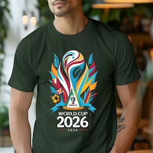 May include: Dark green t-shirt featuring a colorful graphic of the World Cup 2026 logo. The design includes a stylized trophy, a soccer ball, and the text "WORLD CUP 2026". The shirt is short-sleeved.