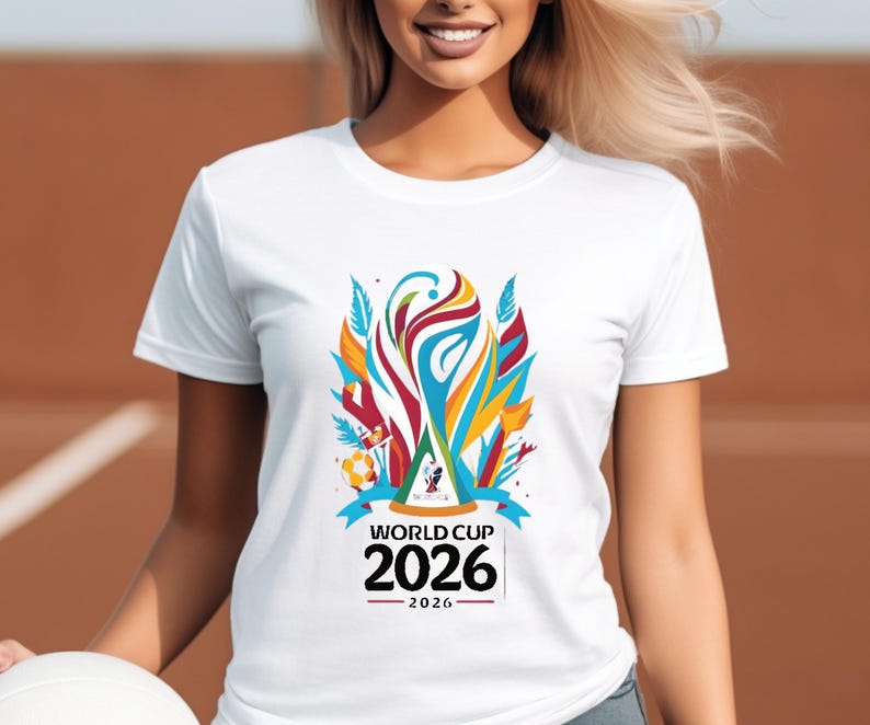 May include: White t-shirt featuring a colorful graphic design for the 2026 World Cup. The design includes a stylized trophy, ribbons, and the text "WORLD CUP 2026". The shirt is made of a soft material.
