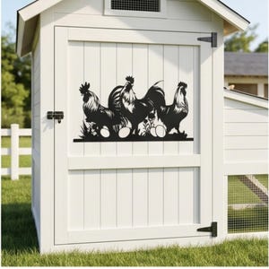 May include: A white chicken coop door features a black metal silhouette of three roosters, eggs, and foliage. The door has vertical wooden panels and black hinges and a latch. The coop is set on a grassy lawn.