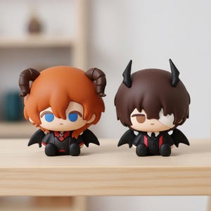 Puede incluir: Dos pequeñas figuras con rasgos diabólicos. Una tiene cabello castaño rojizo y cuernos curvos, la otra tiene cabello castaño y cuernos puntiagudos. Ambas visten trajes negros con detalles rojos, alas negras y rostros estilizados.