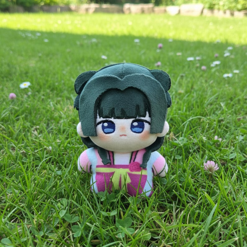 Pu&ograve; includere: Una bambola di peluche con una copertura per la testa verde a forma di capelli e un abito rosa e viola. La bambola ha grandi occhi blu ed &egrave; seduta in un'area erbosa. L'abito della bambola ha un dettaglio a fiocco.