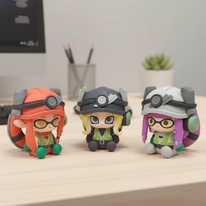 May include: Three colorful figurines of characters wearing miner-style helmets and vests. The figurines have large eyes and are in orange, gray, and white. The figurines are sitting on a light-colored wooden surface.