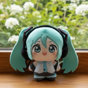 May include: A plush doll featuring a character with long teal hair in twin tails, wearing black headphones, a white collared shirt with a light blue tie, and dark gray shorts. The character has large teal eyes, a small open mouth, and pink cheeks.