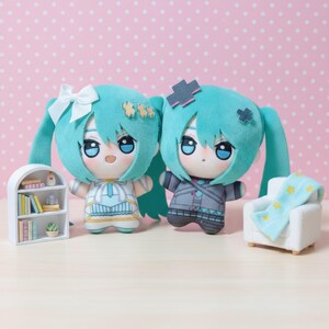 May include: Two plush dolls with teal hair and large blue eyes, each in a different outfit. One doll is dressed in white and gold, the other in grey and blue. A miniature white bookshelf and armchair with a star-patterned blanket are also visible.