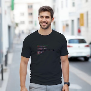 Peut inclure: T-shirt noir avec du texte de code vert et rouge. Le texte sur le t-shirt semble être du code de programmation. Le t-shirt est de style col rond et est fait d'une matière douce. Le t-shirt est porté par une personne.