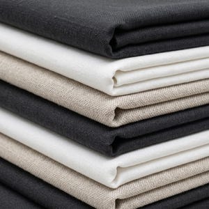 May include: A close-up of a stack of folded linen fabric in shades of grey, white, and beige. The fabric has a textured appearance, suggesting a natural weave. The layers are neatly stacked, showcasing the different colours and textures.