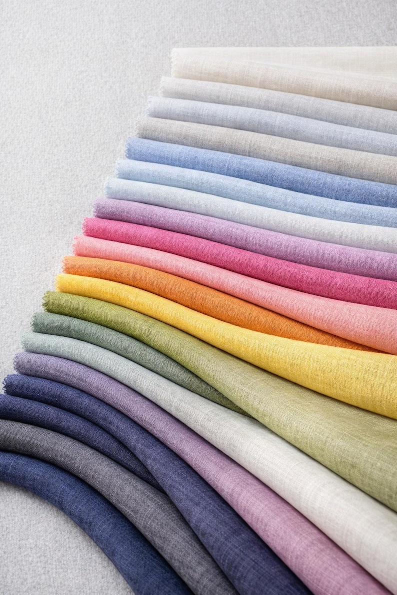 May include: A collection of folded fabric swatches in a spectrum of colors, including shades of blue, pink, orange, yellow, and green. The fabric appears to be linen or a similar material, with a slightly textured surface. The swatches are arranged in a diagonal pattern.