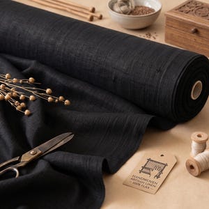 May include: A roll of black linen fabric with a tag that reads "Handwoven Artisan Linen 100% Flax." Also shown are scissors, wooden spools of thread, a small wooden box, and other craft supplies.