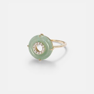 May include: A gold ring featuring a light green jade disc with a central circle of small, sparkling diamonds. The ring has a delicate band and a minimalist design, perfect for everyday wear.