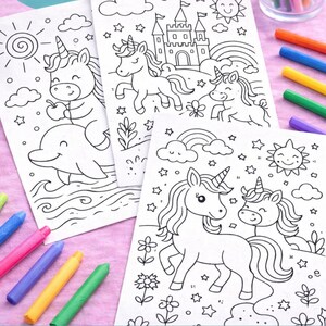 K&ouml;nnte beinhalten: Drei Ausmalbilder mit Einhorn-Motiven, einem Delphin, einer Burg, einem Regenbogen und einer Sonne. Buntstifte in verschiedenen Farben liegen um die Seiten herum, bereit zum Ausmalen. Die Illustrationen sind schwarz auf wei&szlig;em Papier.