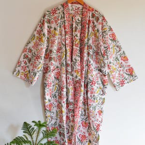May include: A white floral print robe with red, pink, yellow, and green accents. The robe features a long, open design with a matching floral pattern on the trim and pockets. The robe is made of a lightweight fabric.