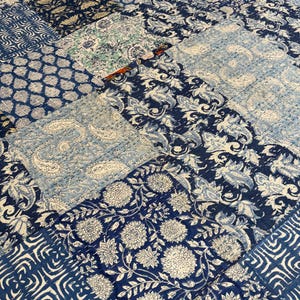 May include: A patchwork quilt featuring a variety of blue and white floral and geometric patterns. The quilt is made of multiple fabric squares stitched together, creating a textured and visually appealing design. The color palette is primarily shades of blue and white.