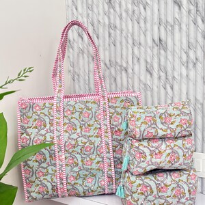 Könnte beinhalten: Eine Tragetasche und drei passende Kosmetiktaschen. Die Taschen haben ein Blumenmuster in Rosa und Grün auf hellblauem Hintergrund. Die Tragetasche hat rosa Griffe und Verzierungen. Die Kosmetiktaschen haben blaue Quasten.