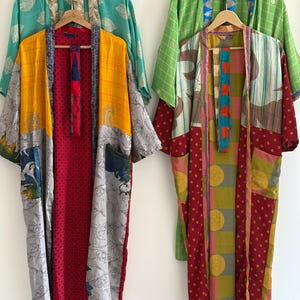 May include: Three colorful, patterned kimonos hanging on wooden hangers. The kimonos feature a variety of colors, including yellow, red, green, and gray. The patterns include polka dots, floral designs, and geometric shapes. The kimonos are made of a lightweight fabric.