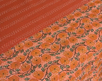 May include: A coral-colored quilt with a floral pattern and a striped design. The floral section features orange flowers with green leaves and brown stems. The striped section has white stitching. The quilt is folded.