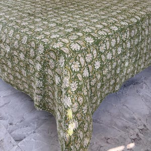 May include: A green and white floral patterned bedspread. The bedspread features a repeating design of paisley and floral motifs. The fabric is a solid green color with white and gold accents. The bedspread is draped over a bed.
