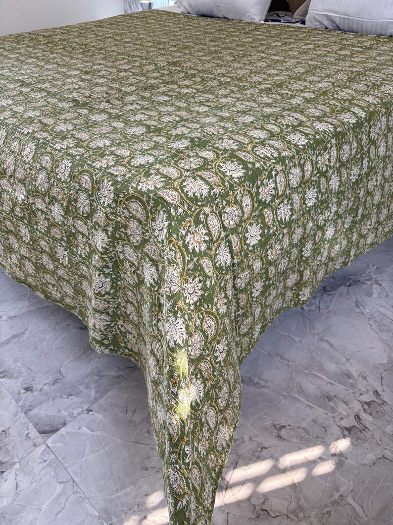 May include: A green and white floral patterned bedspread. The bedspread features a repeating design of paisley and floral motifs. The fabric is a solid green color with white and gold accents. The bedspread is draped over a bed.