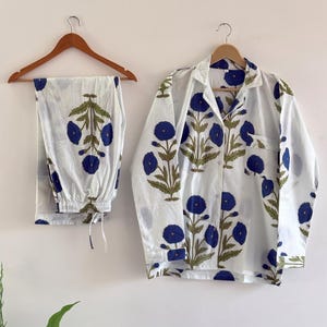 May include: White pajama set with a blue floral pattern. The set includes a button-down shirt with a chest pocket and matching pants. The floral design features blue flowers and green leaves.