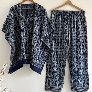 May include: A two-piece pajama set in navy blue with a white floral pattern. The set includes a short-sleeved top and matching pants. The top has a V-neck and a drawstring. The pants have an elastic waistband. The set is hanging on a wooden hanger.