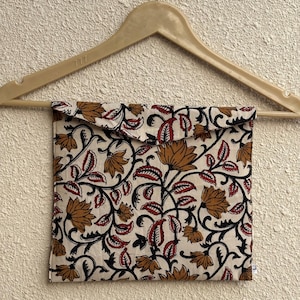 May include: A cream-colored fabric pouch with a floral pattern in brown, red, and black, hanging from a wooden hanger. The pouch features a repeating design of stylized flowers and leaves.