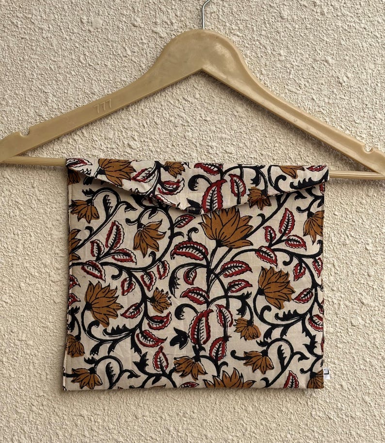 May include: A cream-colored fabric pouch with a floral pattern in brown, red, and black, hanging from a wooden hanger. The pouch features a repeating design of stylized flowers and leaves.