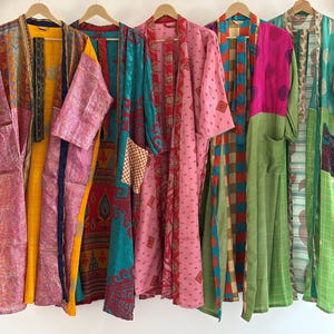 Peut inclure: Une collection de kimonos colorés et à motifs suspendus à des cintres en bois. Les kimonos présentent une variété de couleurs, dont le rose, le vert, le jaune et le turquoise, avec des motifs complexes et des détails de patchwork. Les vêtements sont en tissu léger.
