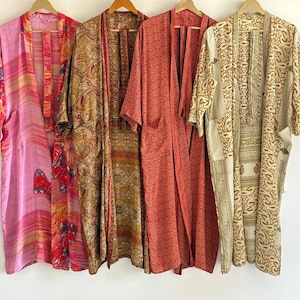 May include: Four colorful, patterned kimonos hang on wooden hangers. The kimonos feature a variety of designs, including floral, paisley, and geometric patterns. Colors include pink, red, gold, and cream. The kimonos are made of a lightweight fabric.