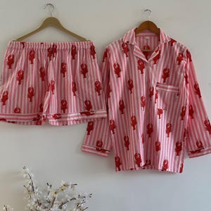 Women's cotton sleepwear set with lobster motifs and pink stripes, showing the button-down top paired with matching lounge shorts against a white wall with flowers.