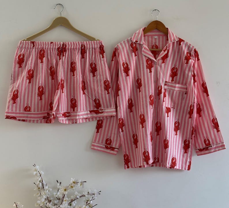 Women's cotton sleepwear set with lobster motifs and pink stripes, showing the button-down top paired with matching lounge shorts against a white wall with flowers.