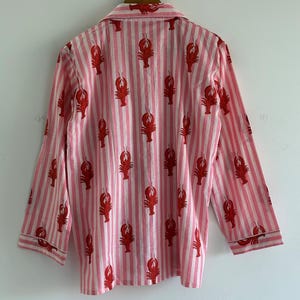 Puede incluir: Camisa de pijama a rayas rosas y blancas con un estampado repetido de langostas rojas. La camisa de manga larga tiene cuello y ribetes blancos en los pu&ntilde;os y el cuello.