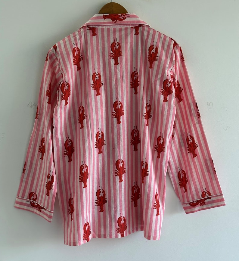 Puede incluir: Camisa de pijama a rayas rosas y blancas con un estampado repetido de langostas rojas. La camisa de manga larga tiene cuello y ribetes blancos en los pu&ntilde;os y el cuello.