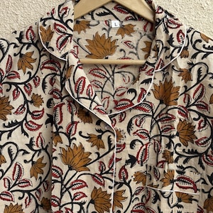 May include: Cream-colored pajama top with a floral pattern in shades of brown, red, and black. The top has a button-down front, a chest pocket, and white piping along the collar and cuffs. The size is L.