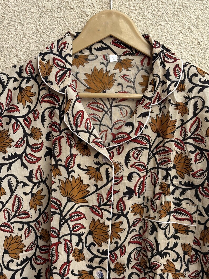 May include: Cream-colored pajama top with a floral pattern in shades of brown, red, and black. The top has a button-down front, a chest pocket, and white piping along the collar and cuffs. The size is L.