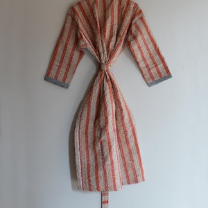 May include: A patterned robe with vertical stripes in shades of orange, beige, and gray. The robe is tied at the waist and has long sleeves with gray cuffs. The robe is hanging on a wooden hanger.
