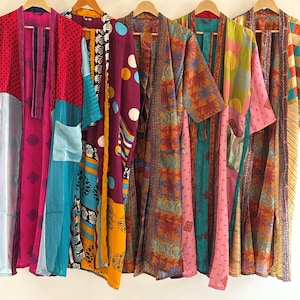 Puede incluir: Una fila de coloridos kimonos estampados colgados de perchas de madera. Los kimonos presentan una variedad de diseños, incluyendo lunares, estampados florales y patrones geométricos. Los colores incluyen rosa, azul, amarillo, naranja y verde. Los kimonos están hechos de tela ligera.