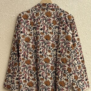 May include: A long-sleeved pajama top with a floral pattern in shades of brown, red, and black on an off-white background. The top is hanging on a wooden hanger. The collar and cuffs have a white trim.