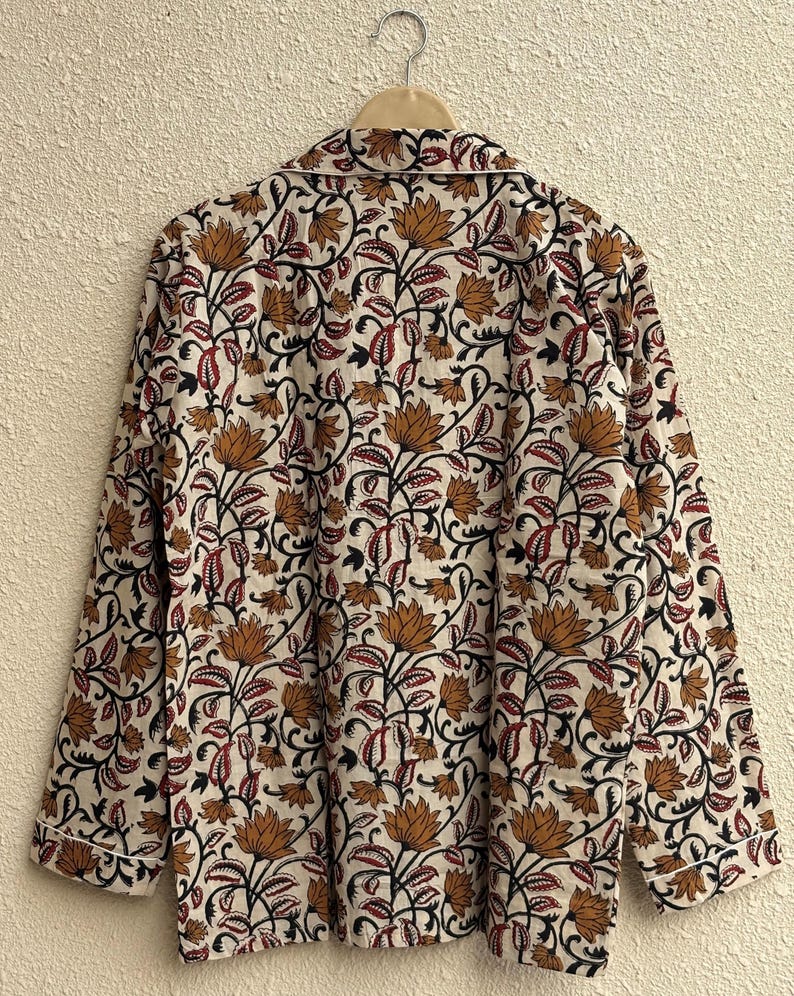 May include: A long-sleeved pajama top with a floral pattern in shades of brown, red, and black on an off-white background. The top is hanging on a wooden hanger. The collar and cuffs have a white trim.