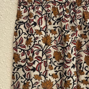 May include: Cream-colored fabric with a repeating floral pattern in shades of brown, red, and black. The design features stylized flowers and leaves on winding vines. The fabric is likely used for clothing or home decor.