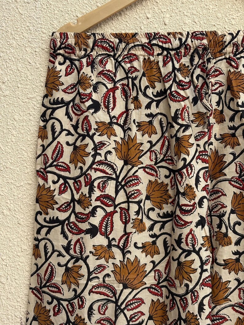 May include: Cream-colored fabric with a repeating floral pattern in shades of brown, red, and black. The design features stylized flowers and leaves on winding vines. The fabric is likely used for clothing or home decor.