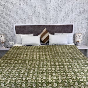 May include: A bed with a green floral patterned quilt, white pillows, and a brown and white striped pillow. The headboard is brown and white. Two lamps with patterned shades sit on bedside tables.