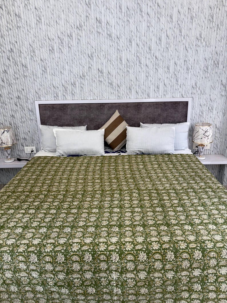 May include: A bed with a green floral patterned quilt, white pillows, and a brown and white striped pillow. The headboard is brown and white. Two lamps with patterned shades sit on bedside tables.