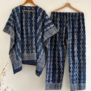 Könnte beinhalten: Zweiteiliger Schlafanzug in Indigo-Blau mit weißem geometrischen Muster. Das Set besteht aus einem locker sitzenden Oberteil mit V-Ausschnitt und einer passenden Hose. Der Stoff scheint leicht zu sein, geeignet für Nachtwäsche oder Loungewear.